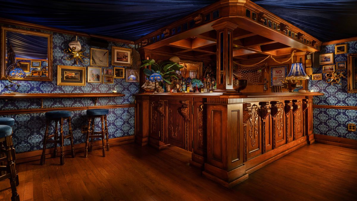 A speakeasy with a wooden bar and blue wallpaper.