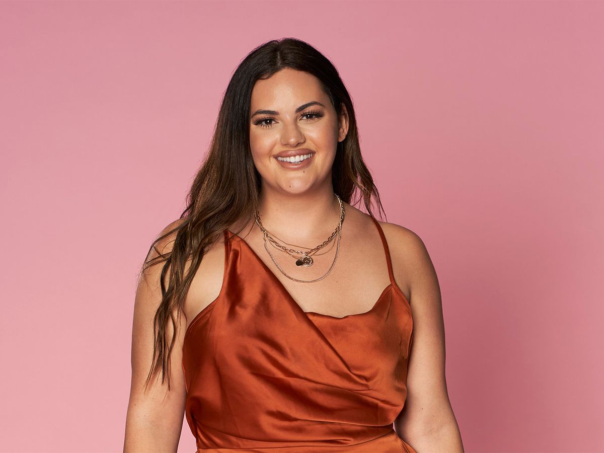 A woman, Alexa Alfia from season 3 of “Love Is Blind” on Netflix, is pictured on a pick background wearing a burnt orange silk dress.