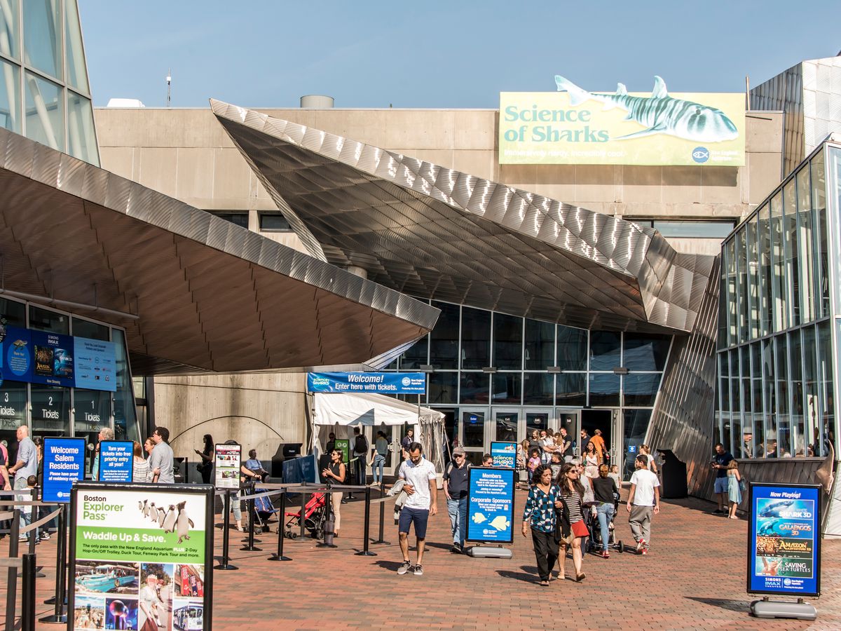 The exterior of the New England Aquarium. There are many people outside. 