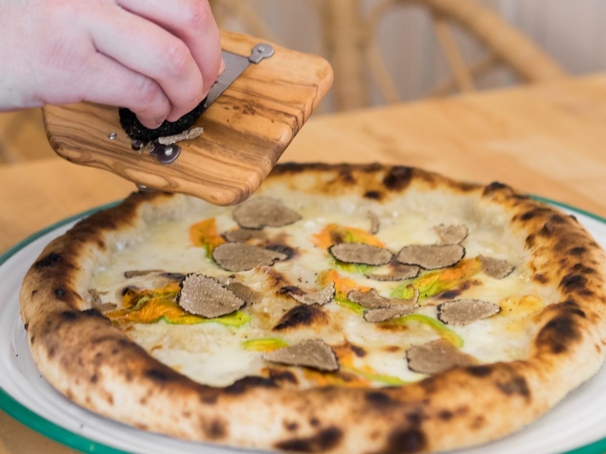Someone shaves black truffles over a pizza.