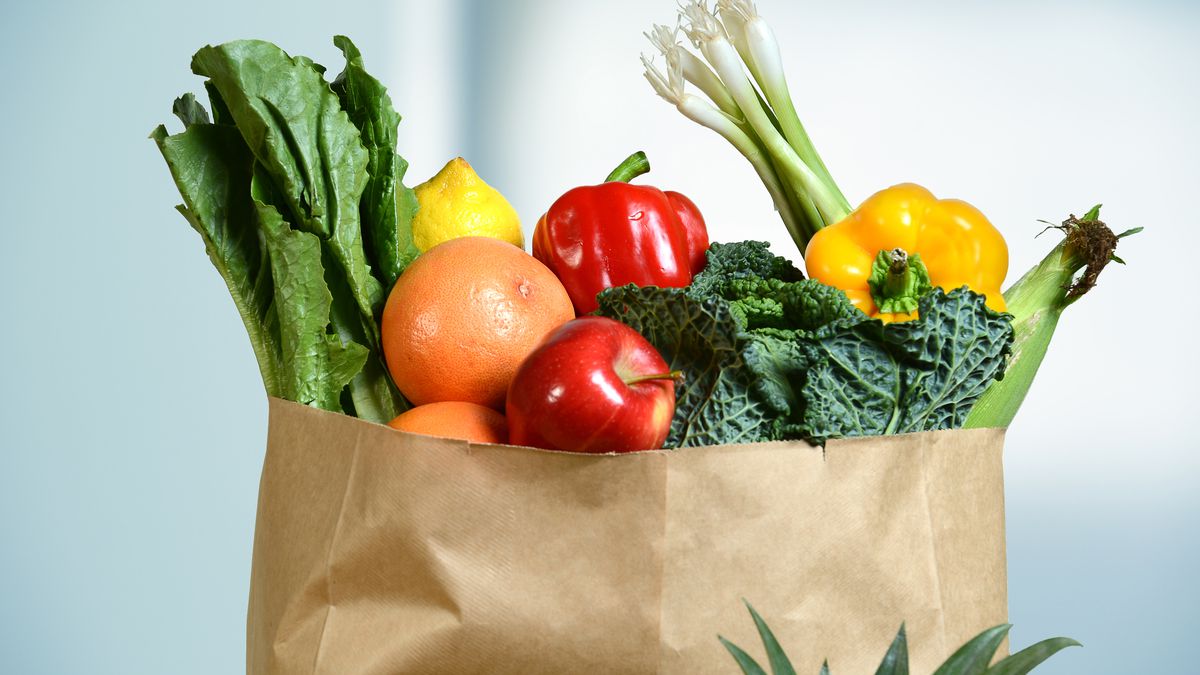 A brown paper bag full of fresh fruits and vegetables is isolated on a light background