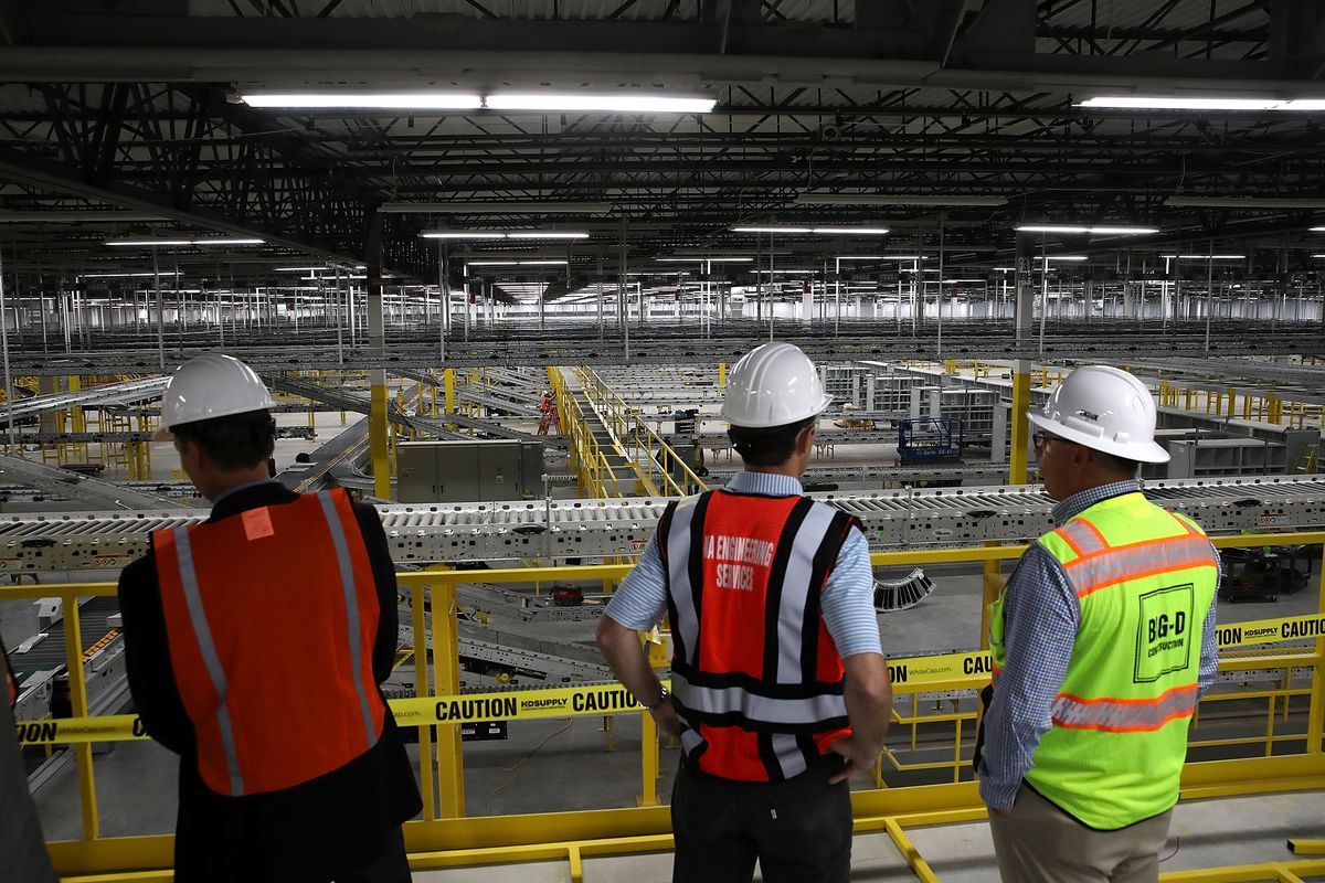 Workers in hardhats and neon vests view a conveyor belt system that is under construction at a new Amazon fulfillment center in Sacramento.