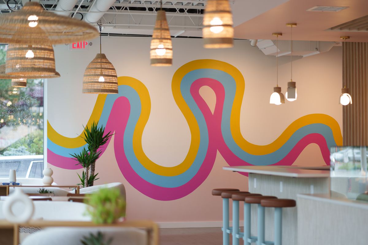 A bright mural of a wave of yellow, pink and blue on a wall. 