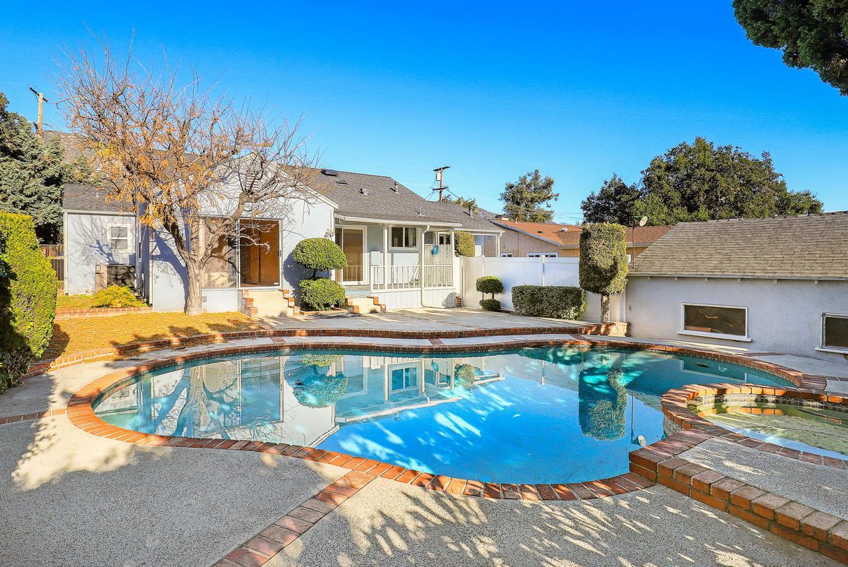 A backyard with a pool dominating the space. In the background is the house and the detached garage. 