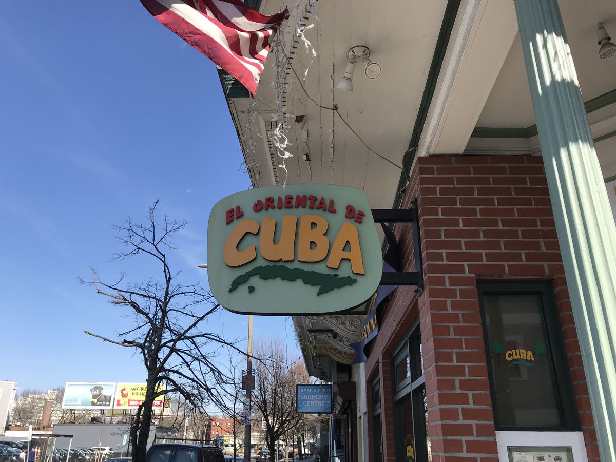 A sign hanging in front of a restaurant reads “El Oriental de Cuba” in pastel colors.