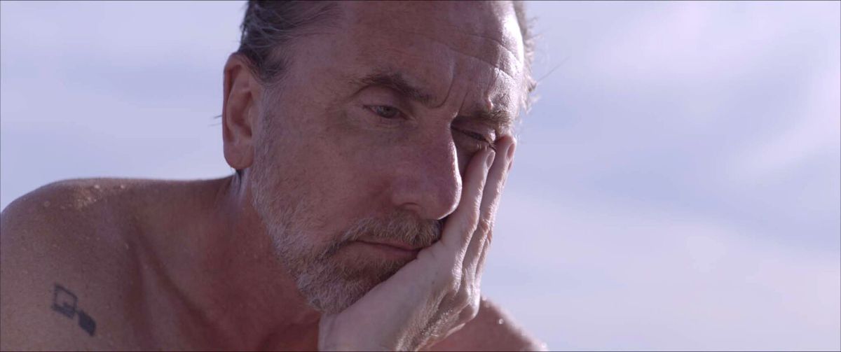 Tim Roth as Neil Bennett looking sullen with his chin resting in his palm in Sundown.