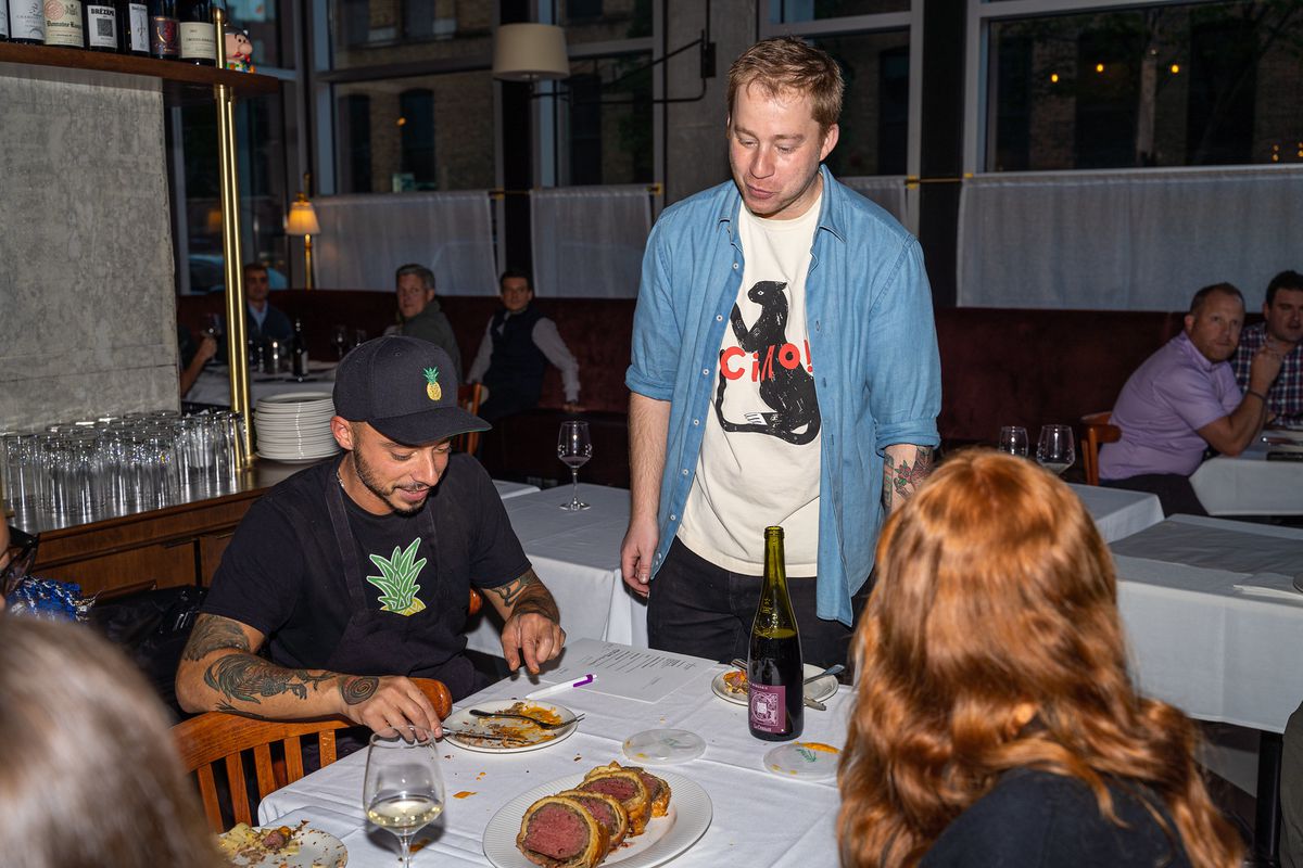 A man stands at a table while two people sit.