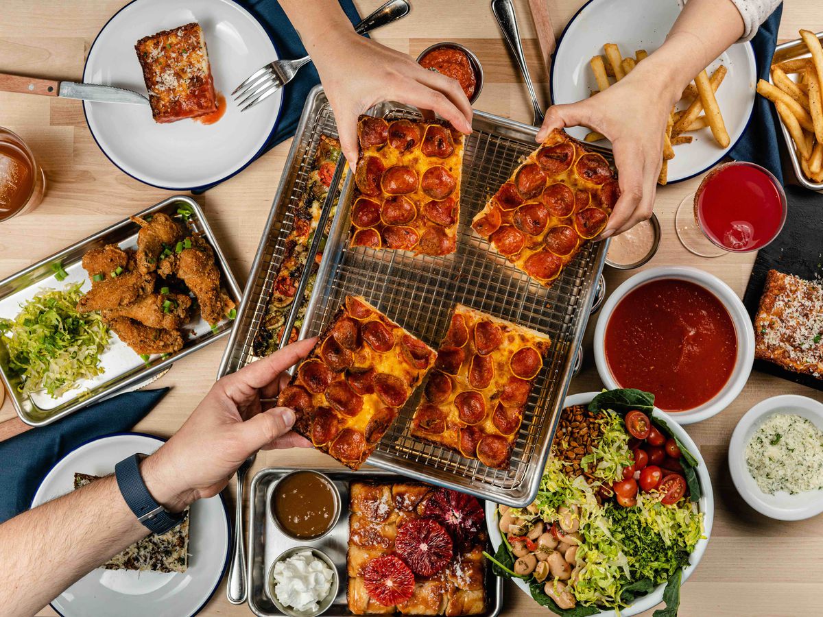 A spread of pizza, salads, and chicken wings at Square Pie Guys