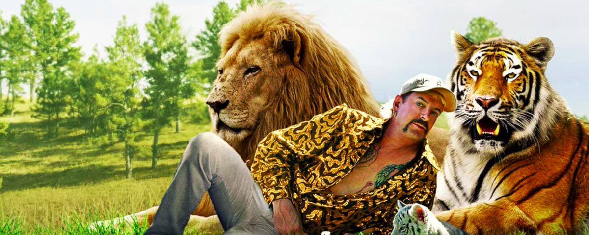 Self-declared Tiger King Joe Exotic, wearing a tiger-striped jacket, lounges on his side in a publicity photo, next to a lion, a bengal tiger, and a white tiger cub.