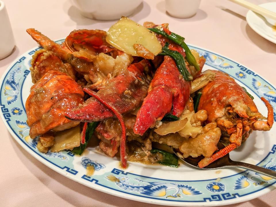A plate with a blue border embellished by birds holds a portion of lobster with scallions and ginger