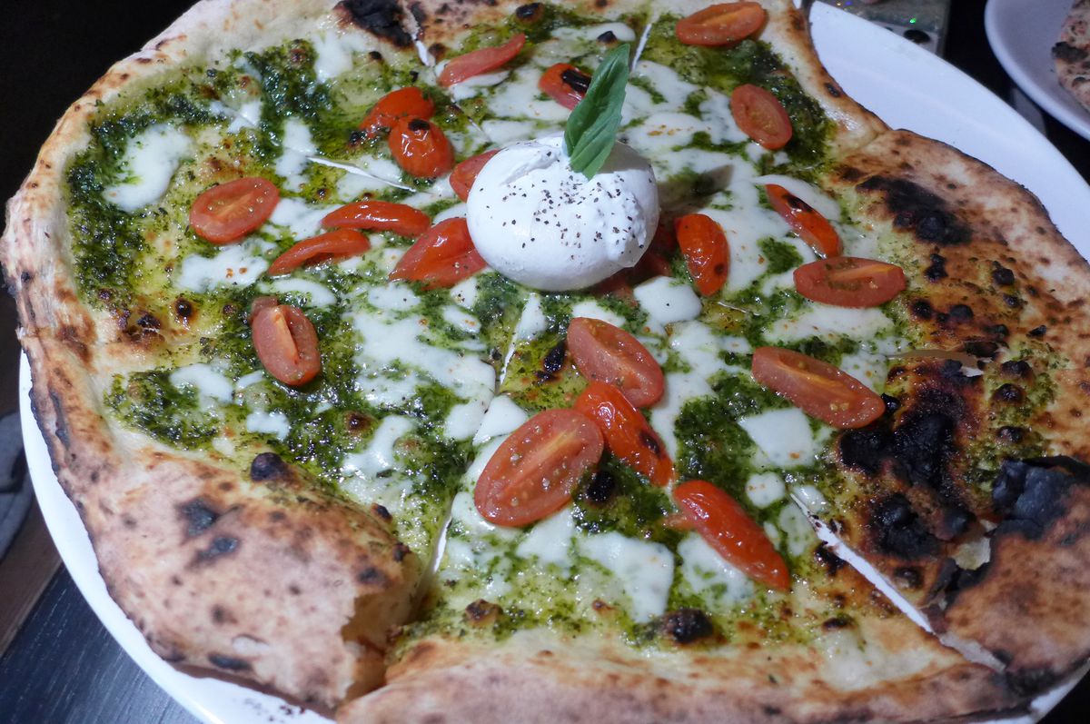 A pizza with green pesto and a ball of burrata in the middle.