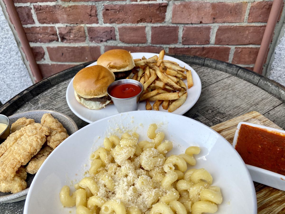 Plates of cheeseburger sliders, fries, and pasta on an outdoor table.
