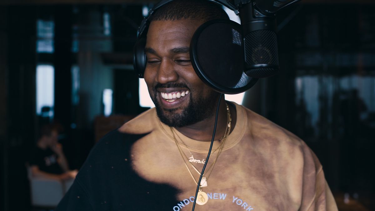 an image from the third episode of jeen-yuhs: A Kanye Trilogy of a headphone-wearing Kanye West smiling in a recording studio, with a microphone and pop filter in front of his face