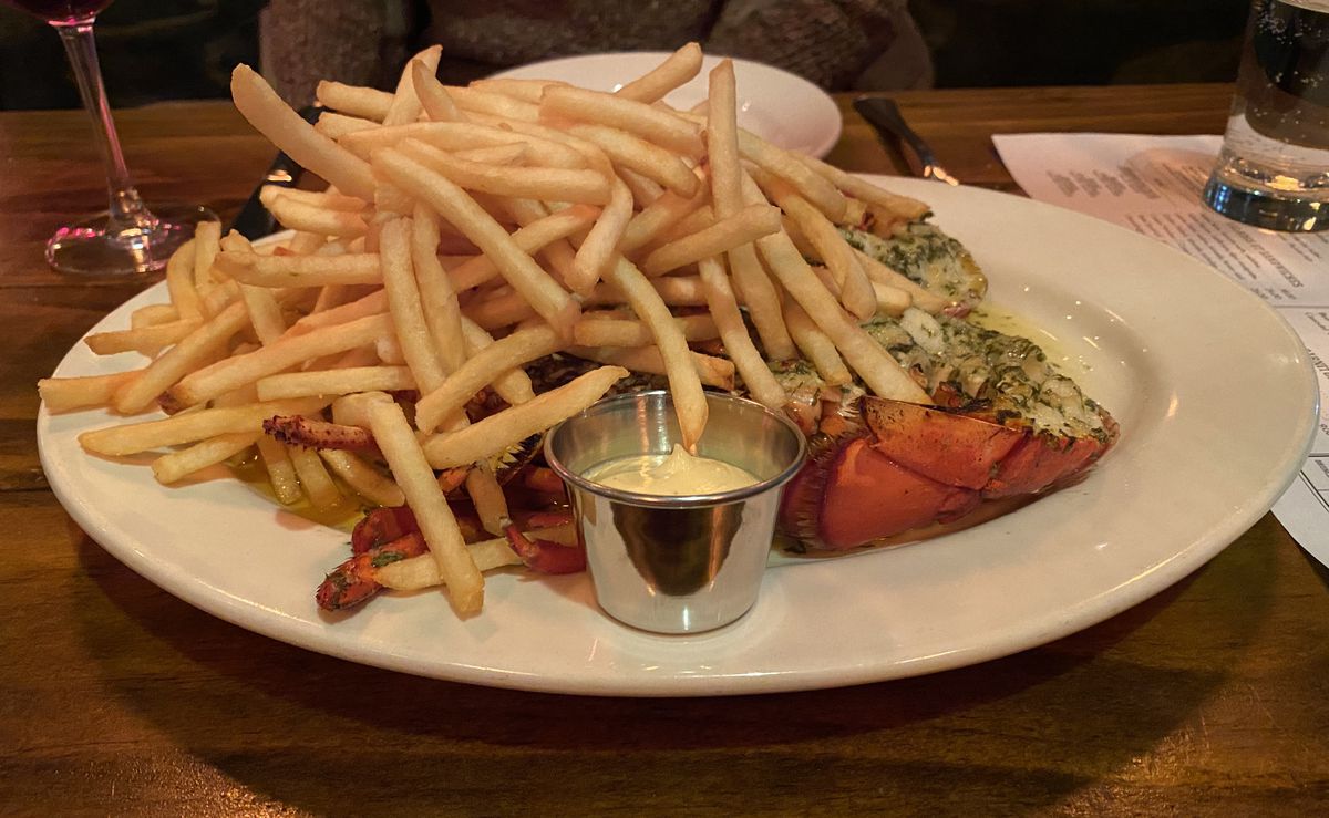 Golden french fries sit atop a split lobster on a white plate