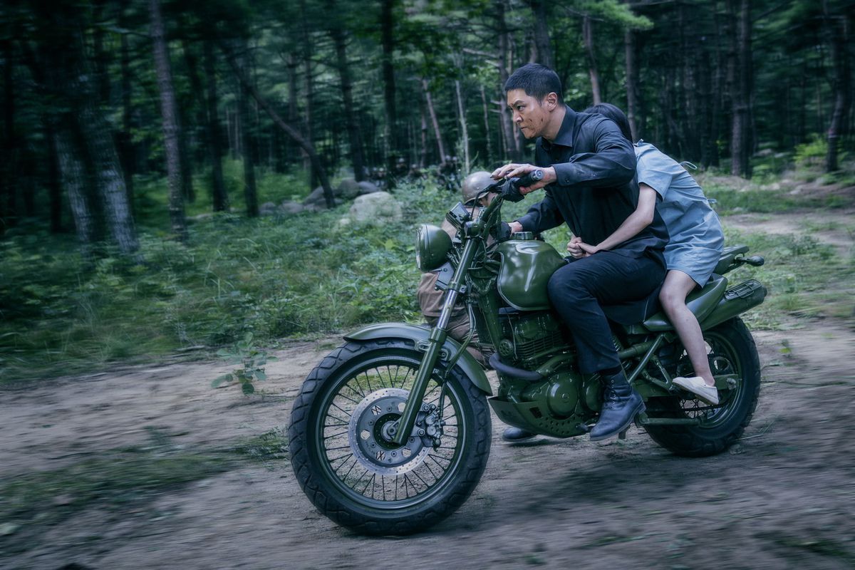 Joo Won as Carter riding a motorcycle through a dense forest in Carter.