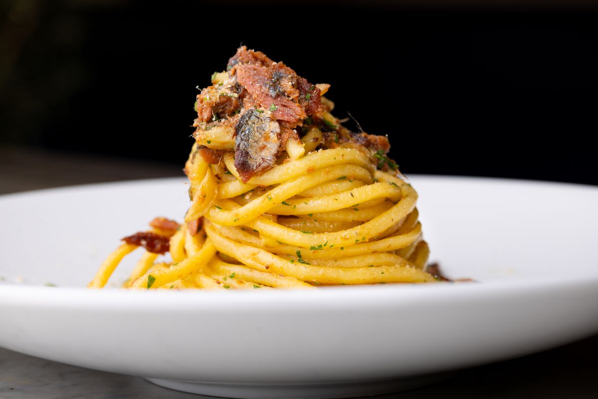 Een close-up shot van dikke spaghettipasta met stukjes oude sardine, lang rondgedraaid, op een wit bord in het nieuwe restaurant Vicini in LA.