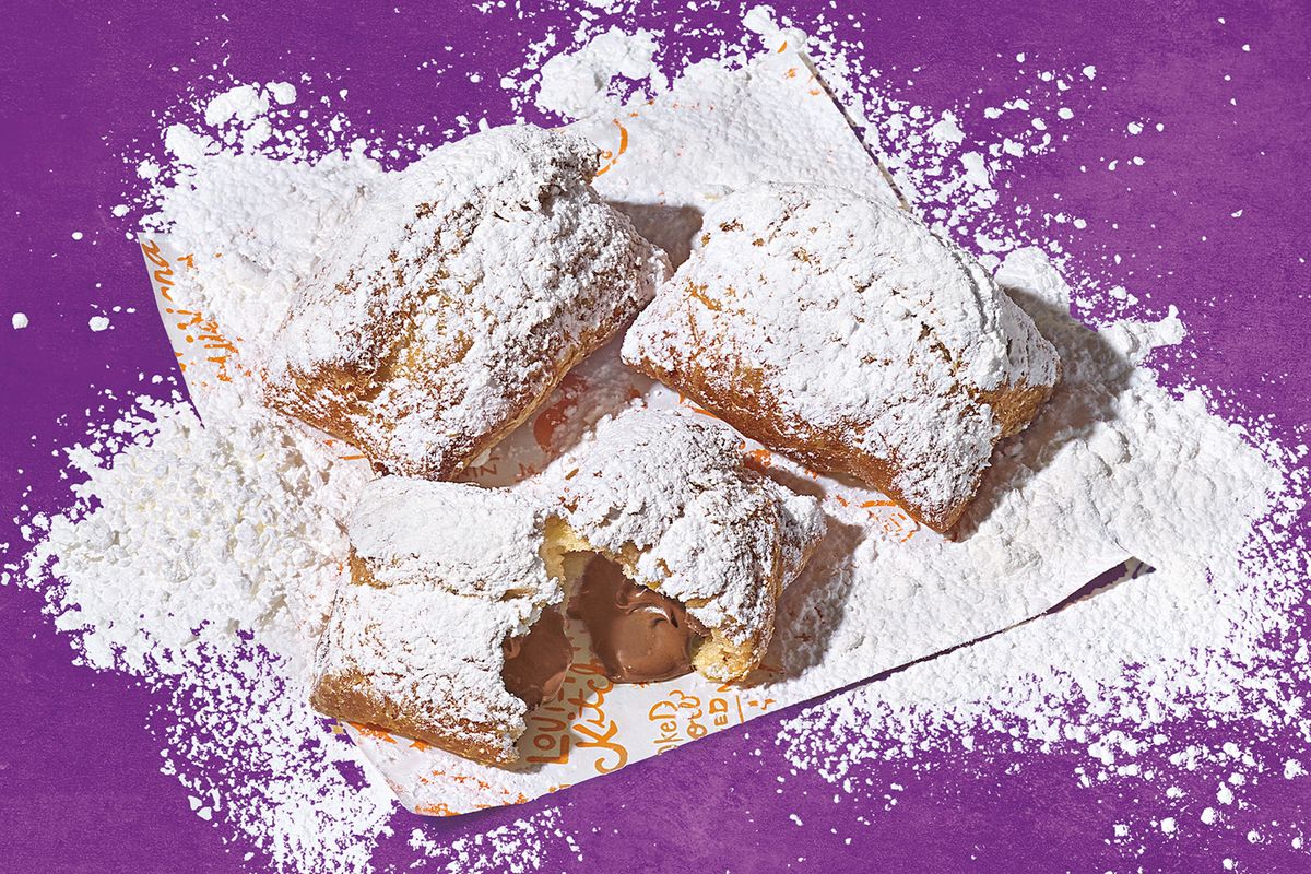 Beignets covered in powdered sugar, scattered on a purple background.