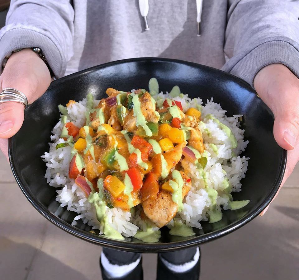 Person holding bowl containing mango basil chicken on rice