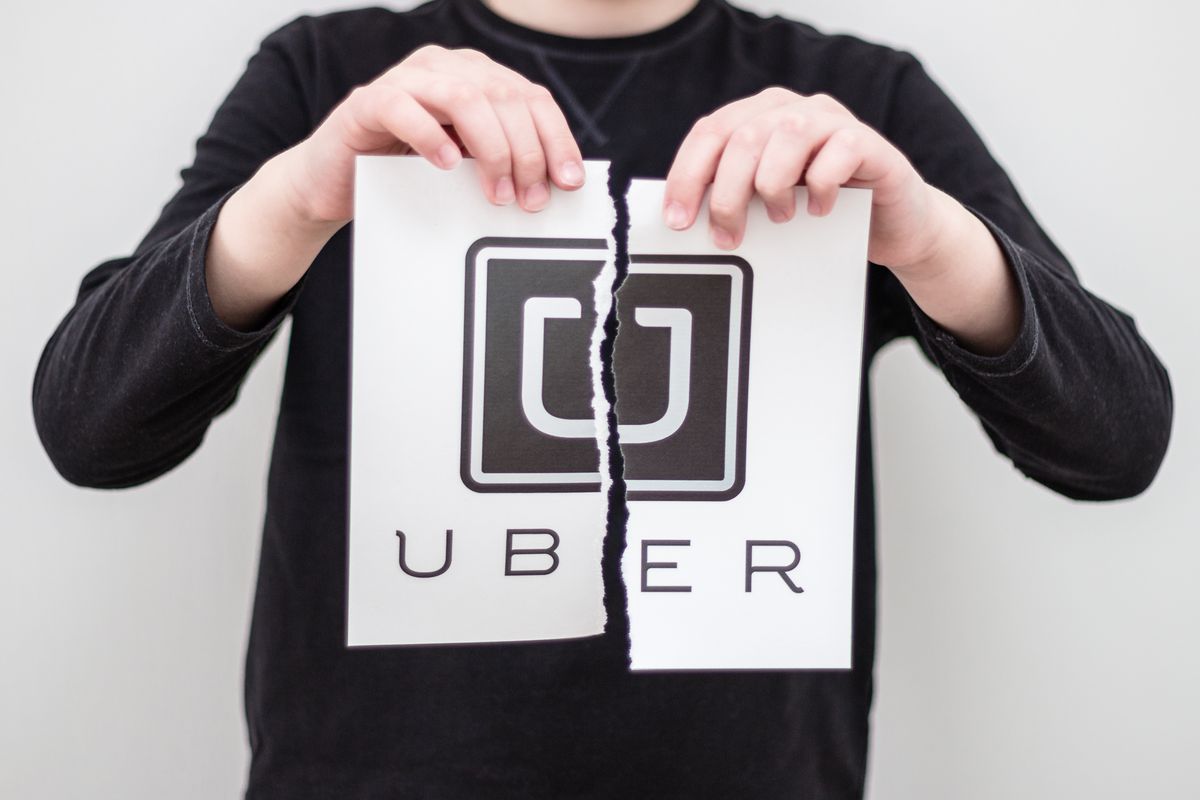Hands tearing the U-shaped Uber logo in half.