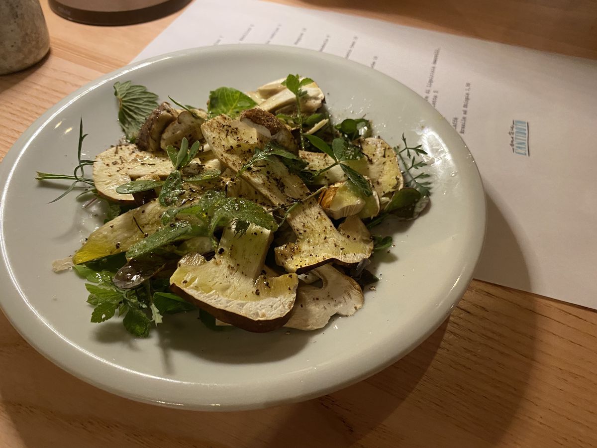 A plate of sliced mushroom salad on a wooden table with a menu beneath the plate
