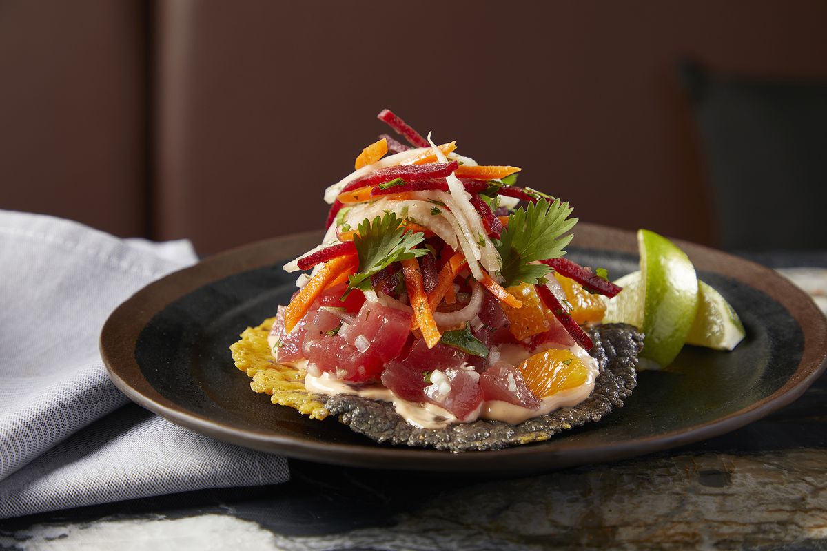 A tortilla on a plate piled high with chunks of fish and strips of vegetables.