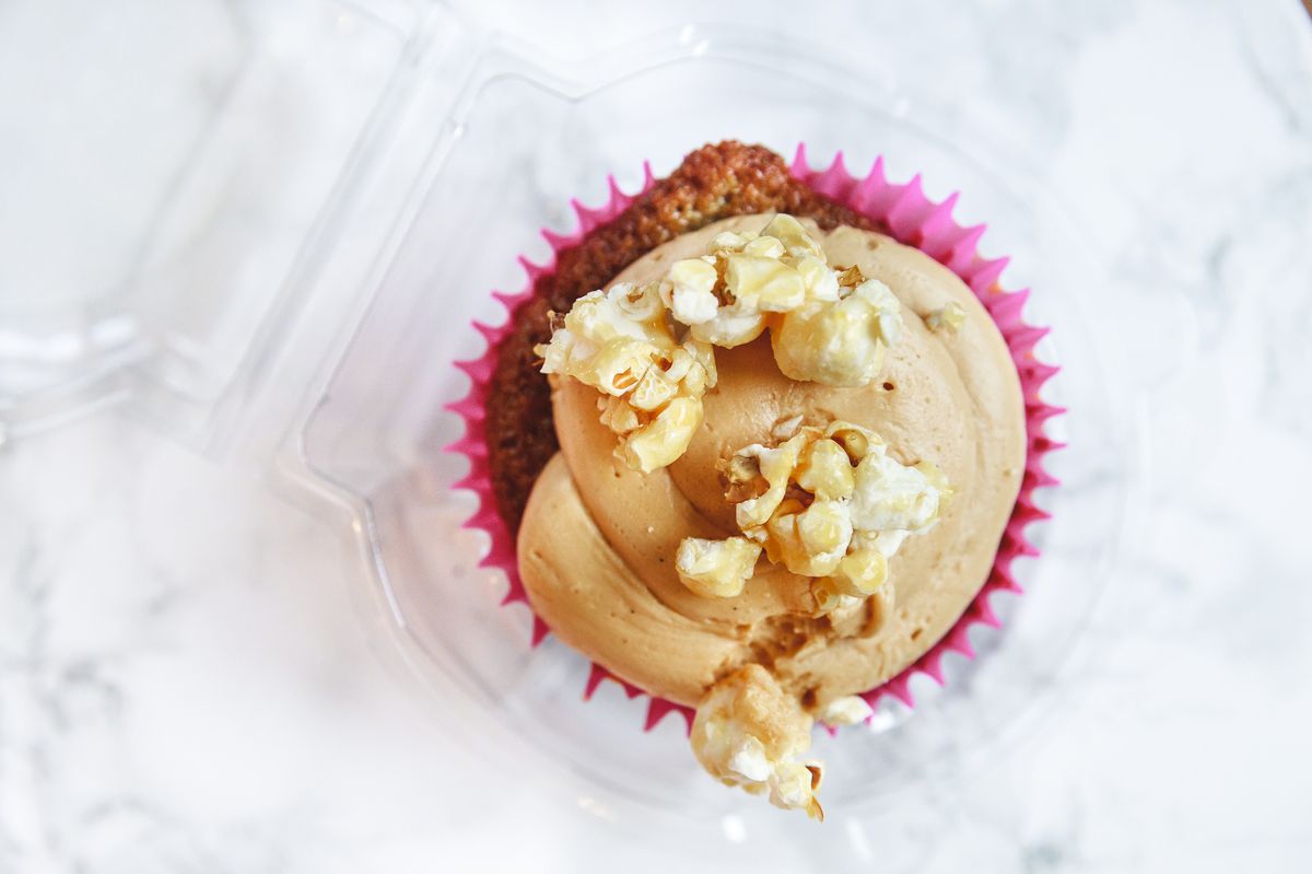 A cupcake in pink paper is topped with caramel-colored frosting and caramel corn