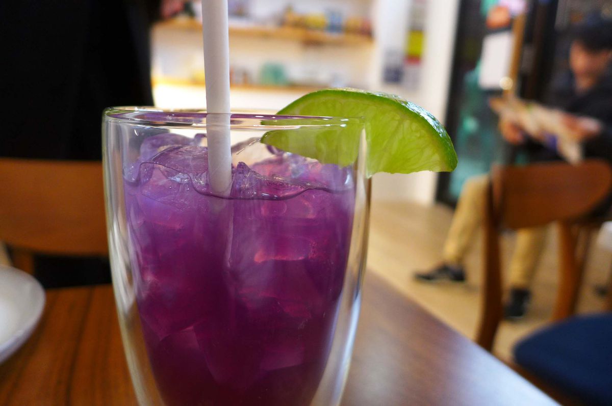 A glass with purple fluid inside and straw sticking out.