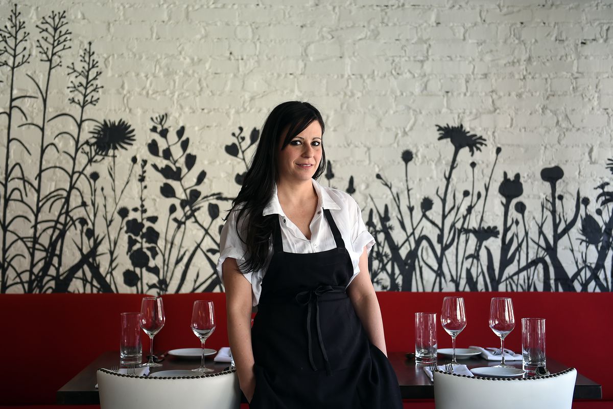 Dirt Candy owner and chef Amanda Cohen stands in a dining room between two set tables and chairs.