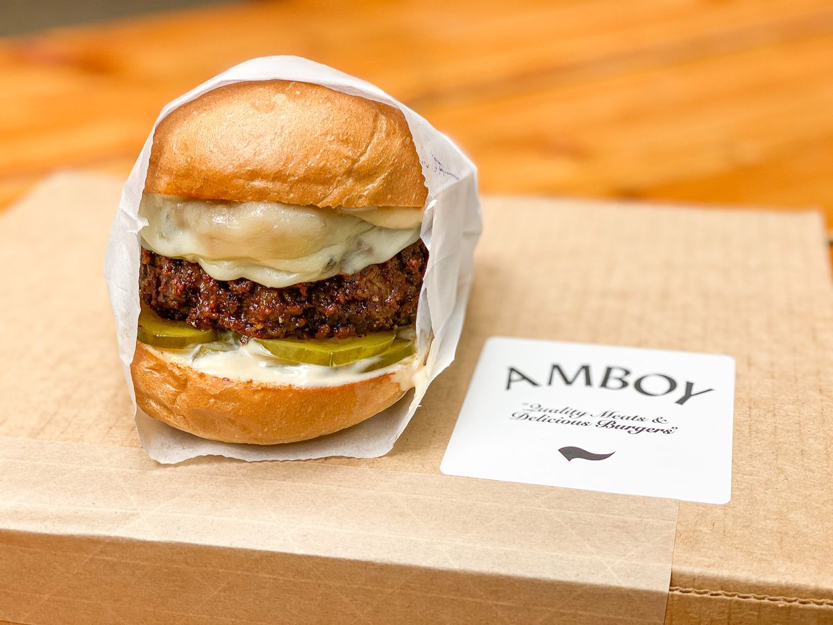 A hamburger wrapped in paper on top of a box that says ‘Amboy.’