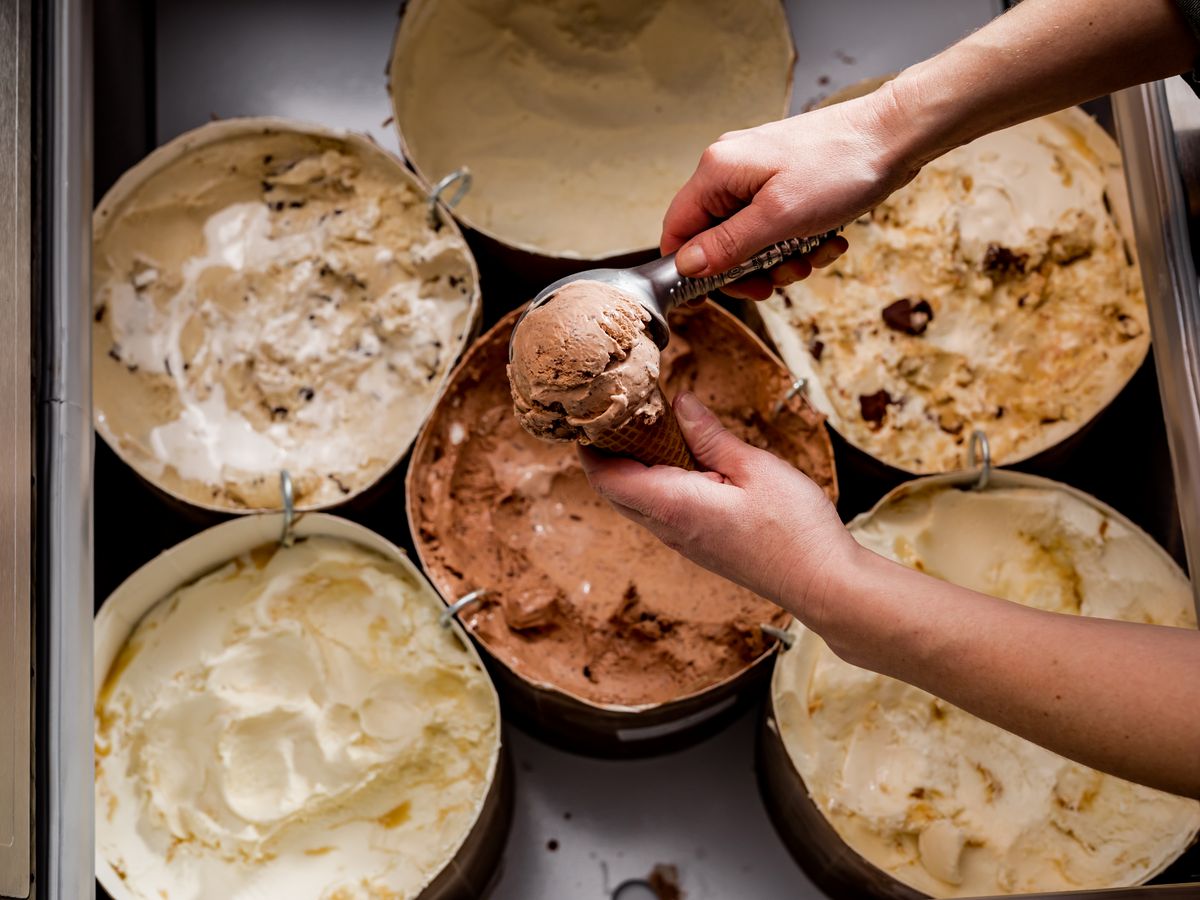 An overhead view of hands scooping ice cream into a cup from a low freezer.