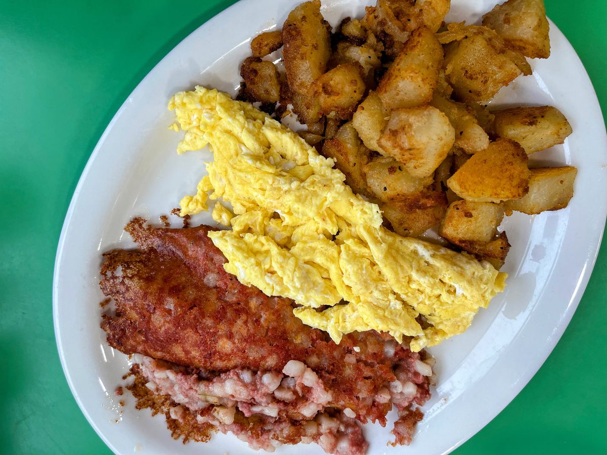A white plate with large portions of hash browns, scrambled eggs, and corned beef hash lined up next to each other on the plate.