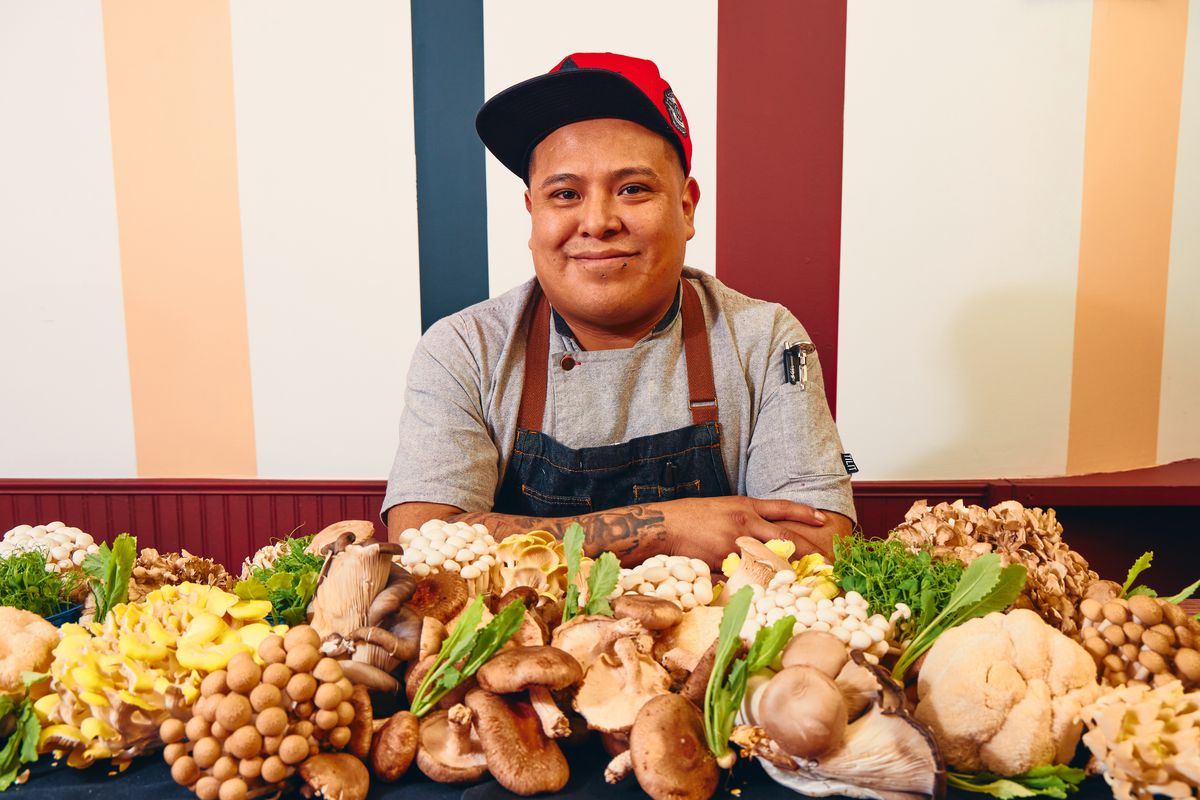 A chef sits among a spread of mushrooms. 