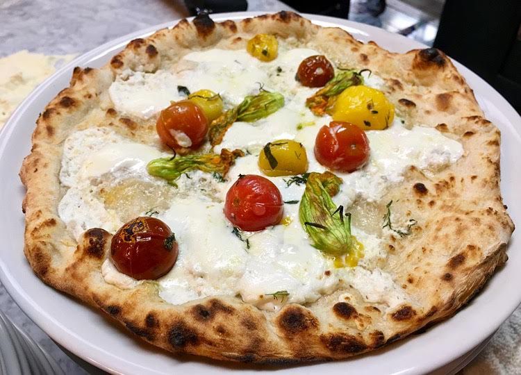 A circular pizza with whole cherry tomatoes and squash blossoms on top.