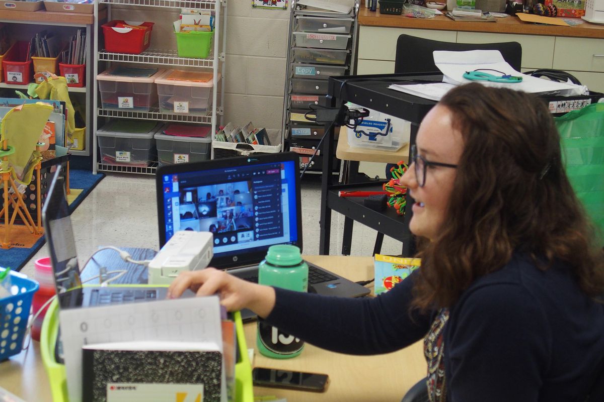 A teacher has two laptops set up at her classroom desk so she can instruct and see her students on videoconference.