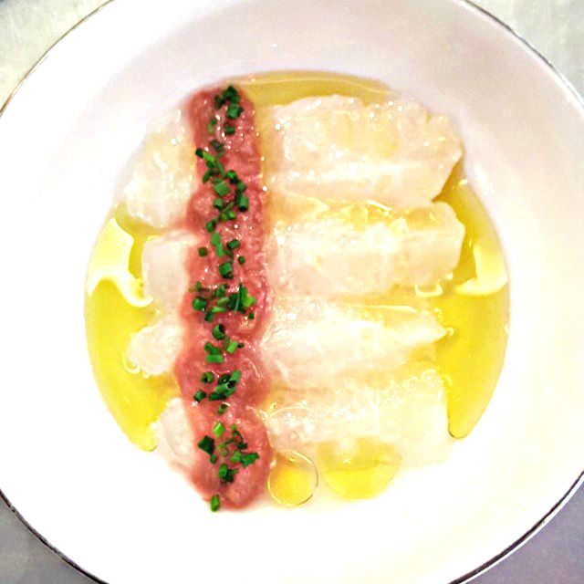 Halibut crudo with filets in a row sitting in a pool of yellow oil.
