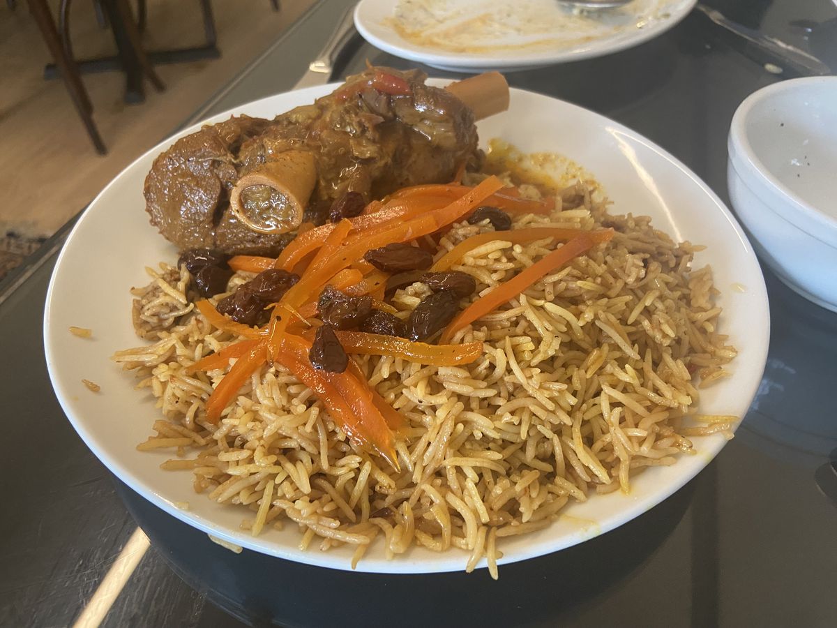 A plate of stewed lamb atop rice with carrots and raisins. 