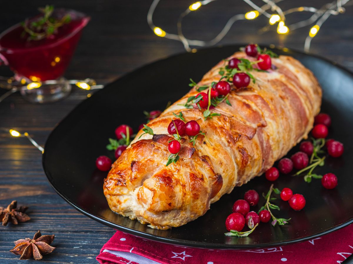 A bacon-wrapped loaf topped with cranberries on a black plate.