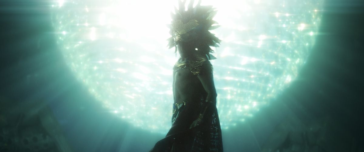 A man in an elaborate feather headdress (played by Tenoch Huerta) and cape swims in front of a gigantic glowing sphere in Black Panther: Wakanda Forever.