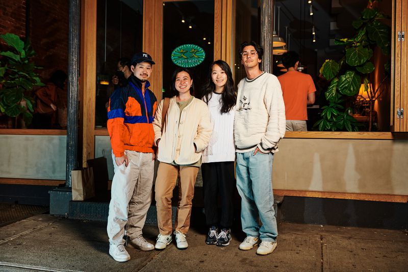 Four people stand next to each other in front of a restaurant with a green sign that says Wenwen.