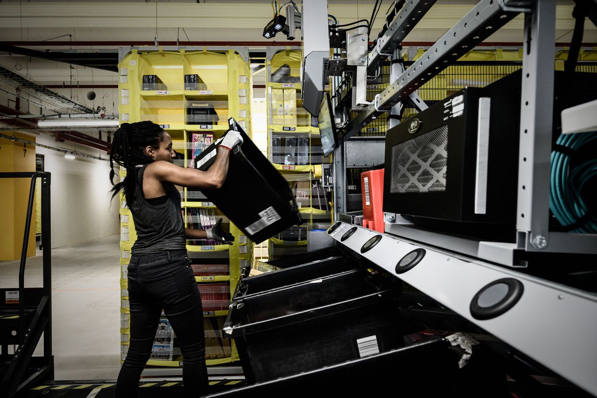 A woman working in an Amazon warehouse lifts a large crate.