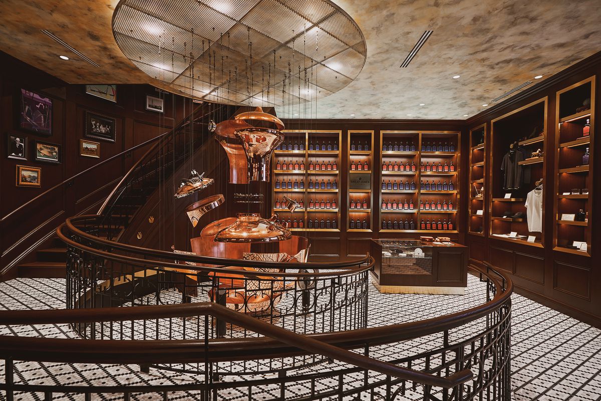 A indoor room with a spiral staircase and dark wooden floor-to-ceiling shelves showcasing bottles of whiskey.