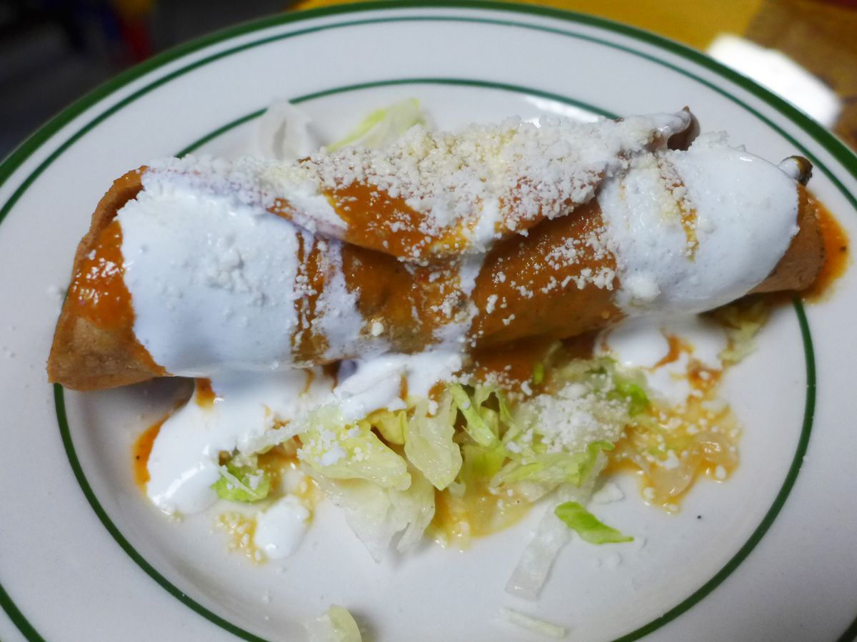 A rolled and fried taco coated with red sauce and topped with sour cream and dried cheese.
