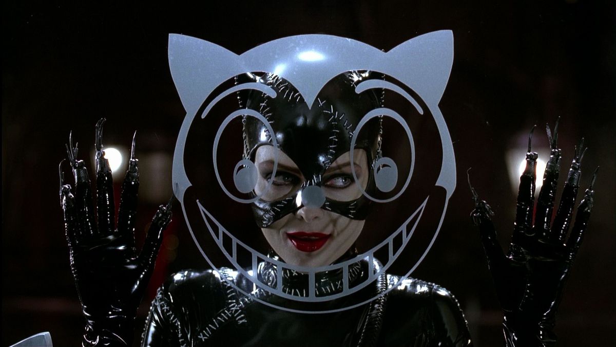 Michelle Pfeiffer as Catwoman in Batman Returns, standing behind a cartoony cat-head image painted on glass