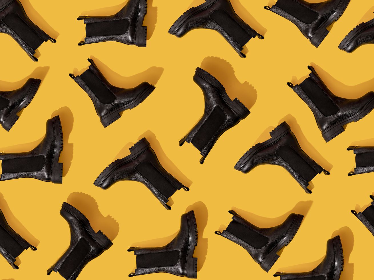 Black ankle boots arranged on a yellow background.