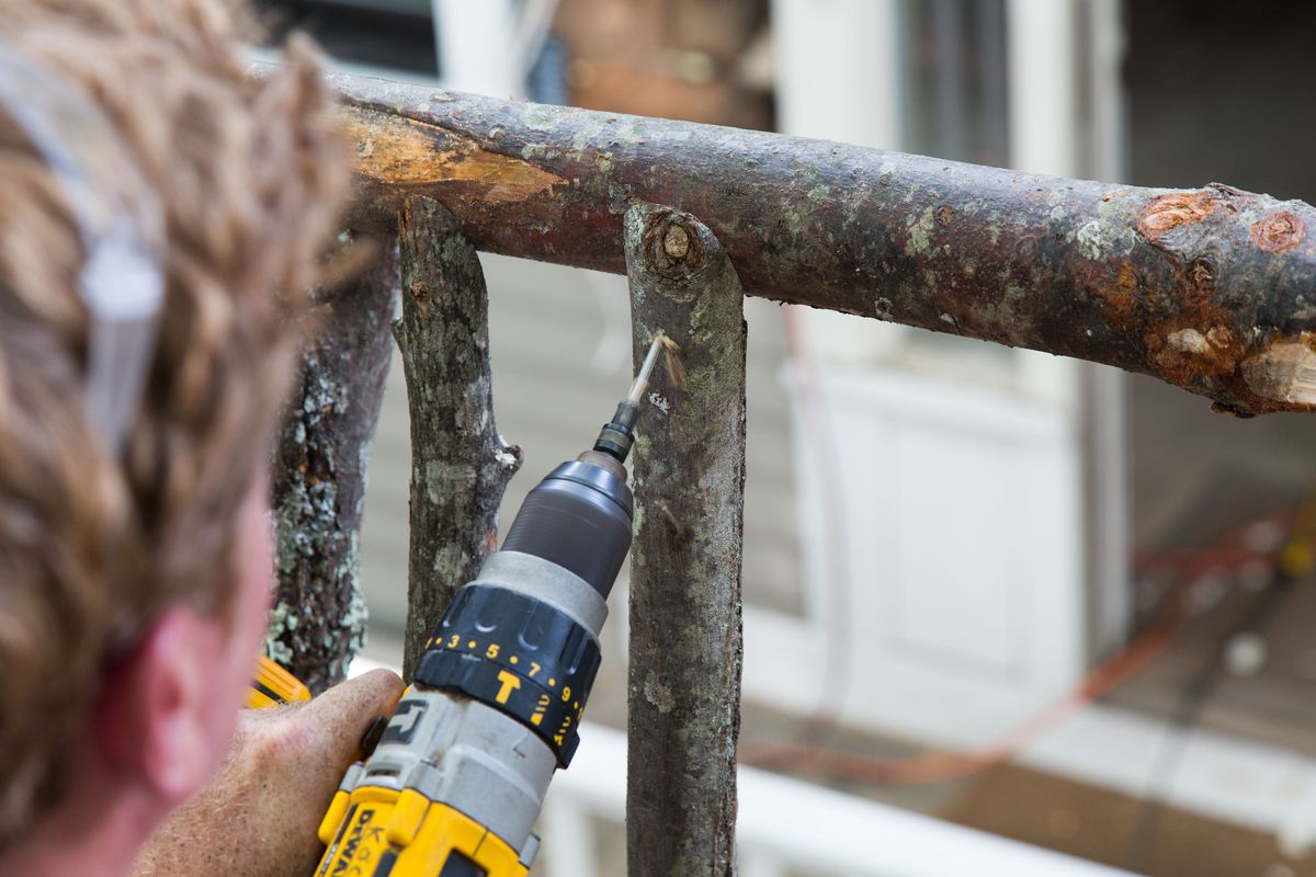 Man Screws In Balusters To Finish Railing Of Tree House