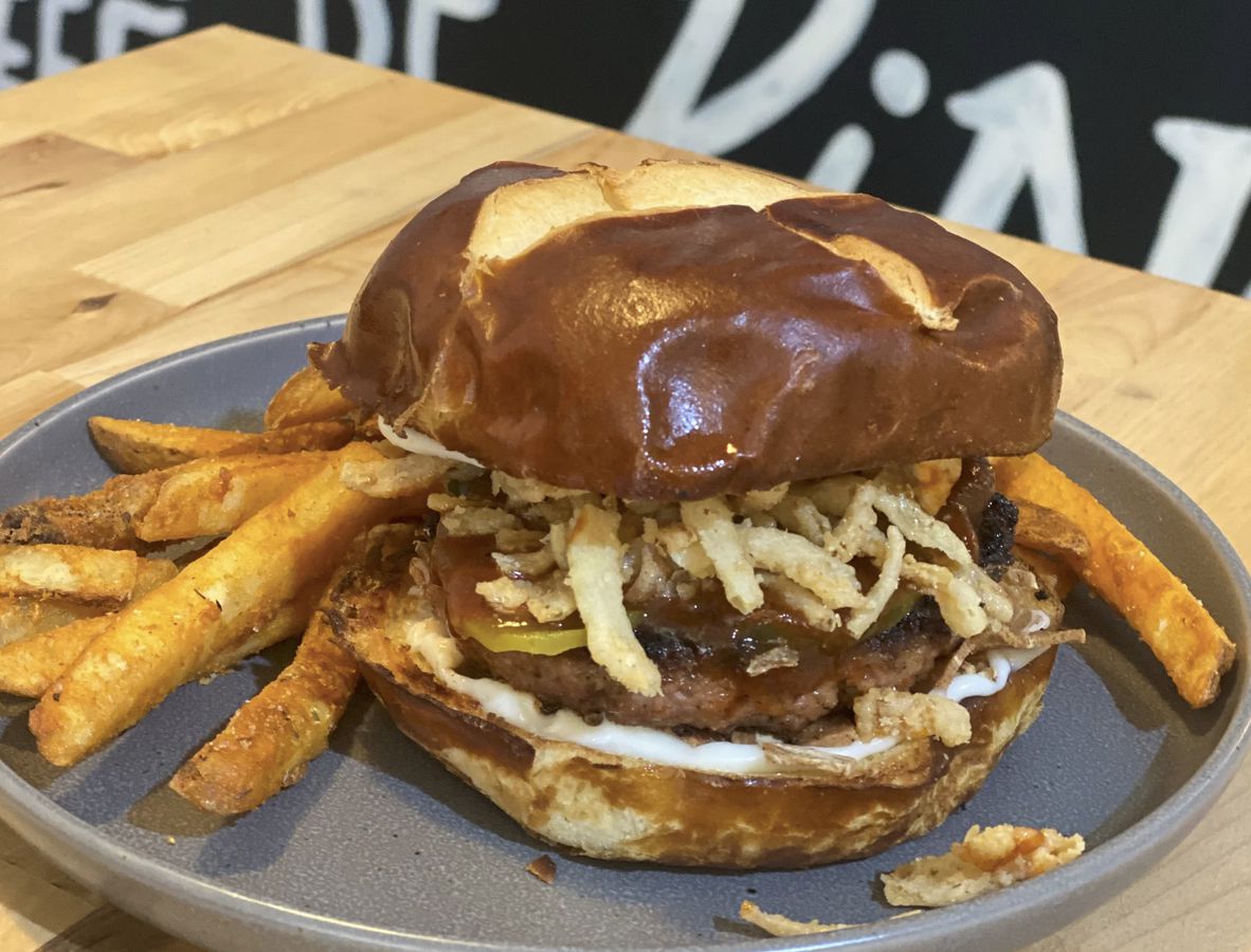 A photo of Homegrown Smoker’s BBQ Bakun Burger with Beyond patty and pretzel bun next to a side of fries.