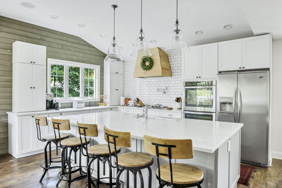 An open kitchen with a large island, three hanging lamps, and white cabinetry.