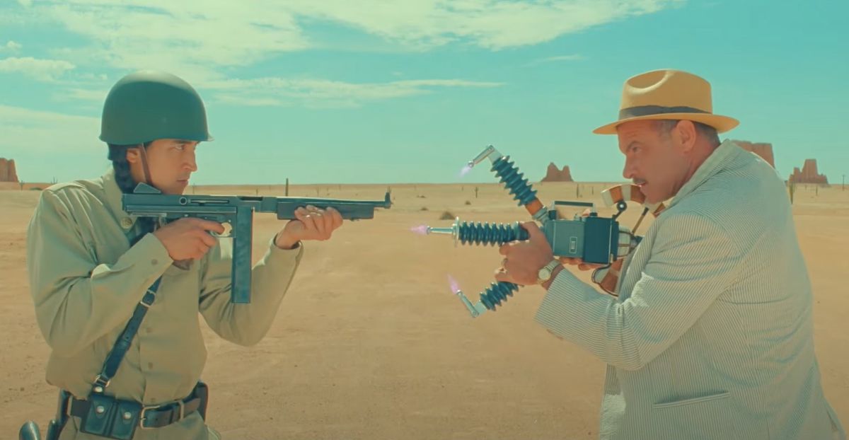 Two men point guns at one another against the backdrop of a desert.