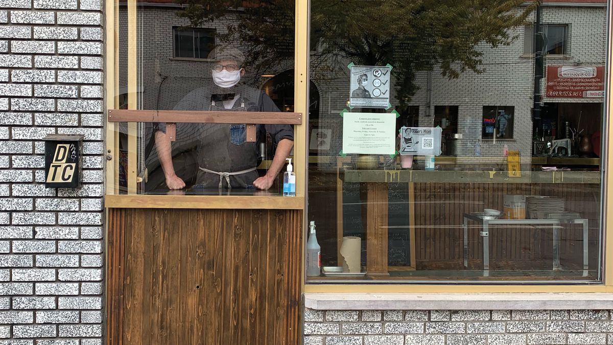 masked man standing behind restaurant window