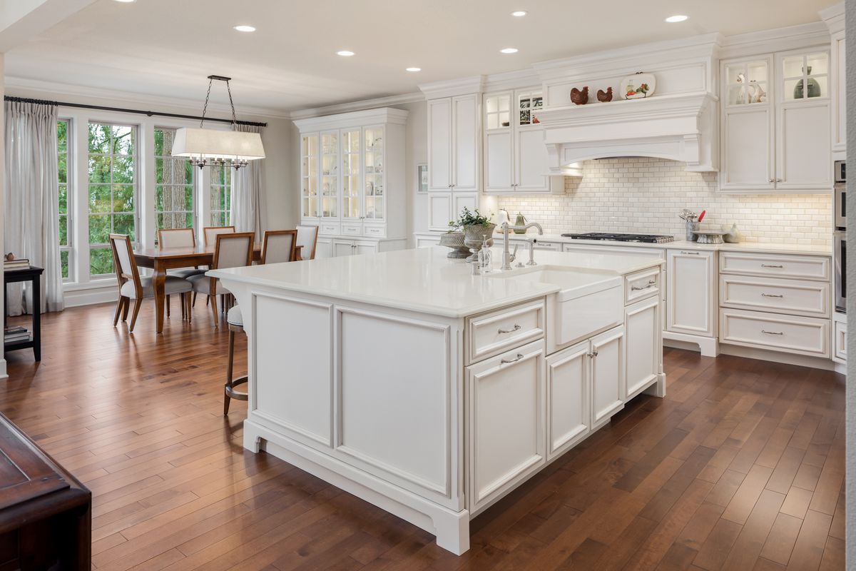 Interior of a home with white kitchen cabinets, white oversized island, wood floors, and long kitchen table. 